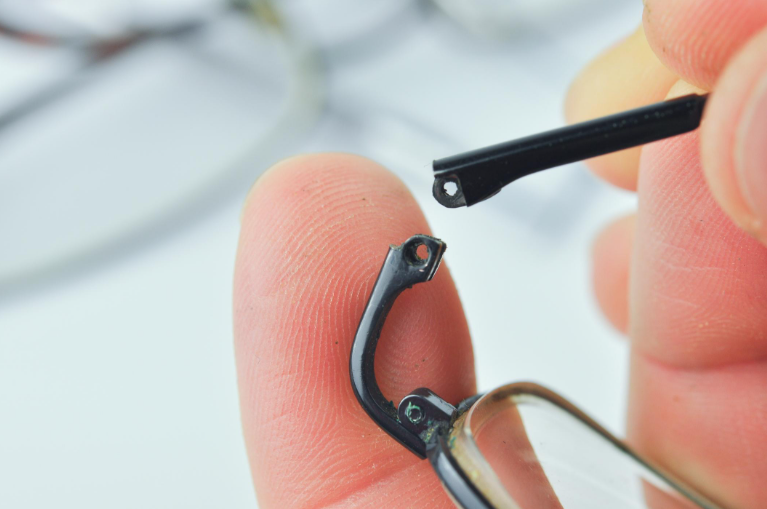 Carefully aligning broken plastic eyeglasses frame pieces during an adhesive repair.