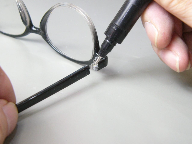 Applying a small amount of compatible adhesive to the broken joint of a plastic eyeglasses frame while protecting the lenses.