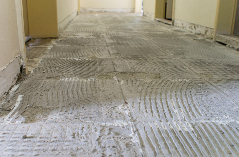 Concrete floor with chipped and uneven patches caused by improper removal of ceramic tiles and tile adhesive.
