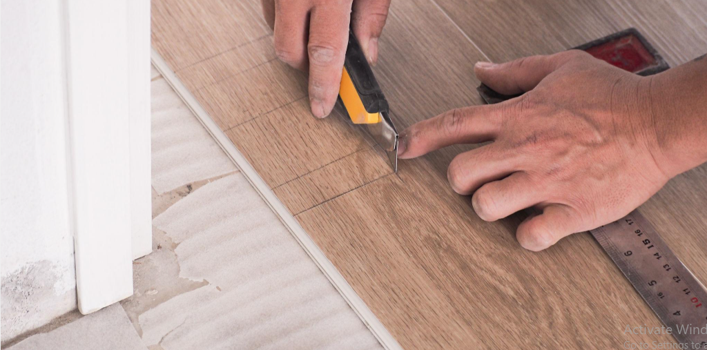 Technician cutting a luxury vinyl flooring plank to size with a utility knife before installation over foam underlayment.