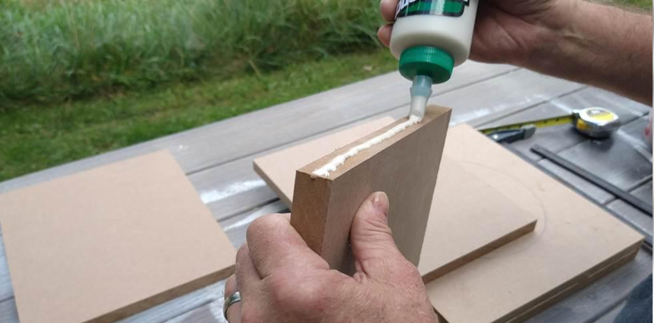 Applying wood glue to the edge of an MDF board before joining it to another board.