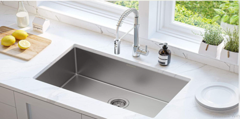 Stainless steel kitchen sink installed in a white marble countertop beneath a bright kitchen window.