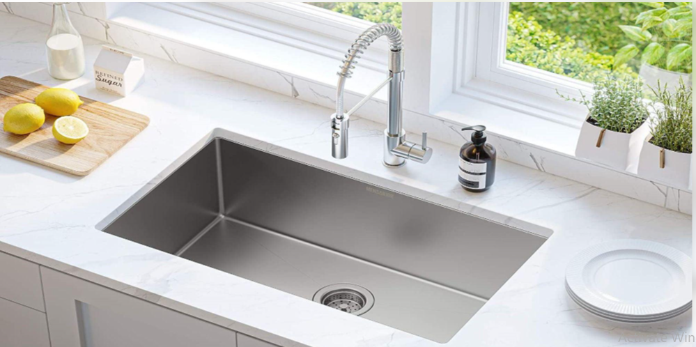 Stainless steel kitchen sink installed in a white marble countertop beneath a bright kitchen window.