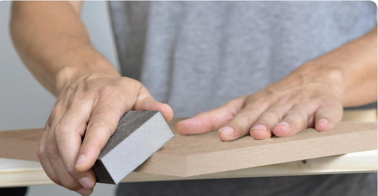 Sanding the edges of an MDF board to remove rough fibres and prepare the surface for wood glue application.