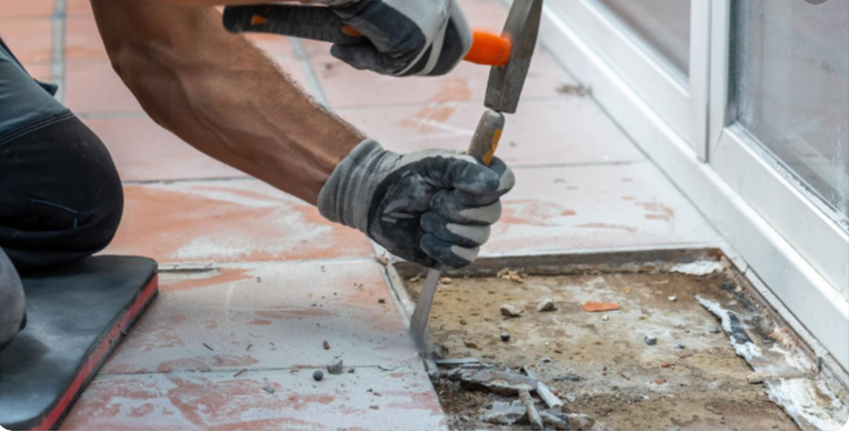 Using a hammer and masonry chisel to carefully lift a ceramic floor tile from concrete without digging into the subfloor.