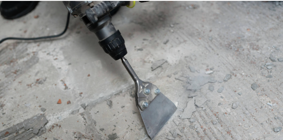 Using a masonry chisel to break hardened thinset tile adhesive away from a concrete floor.