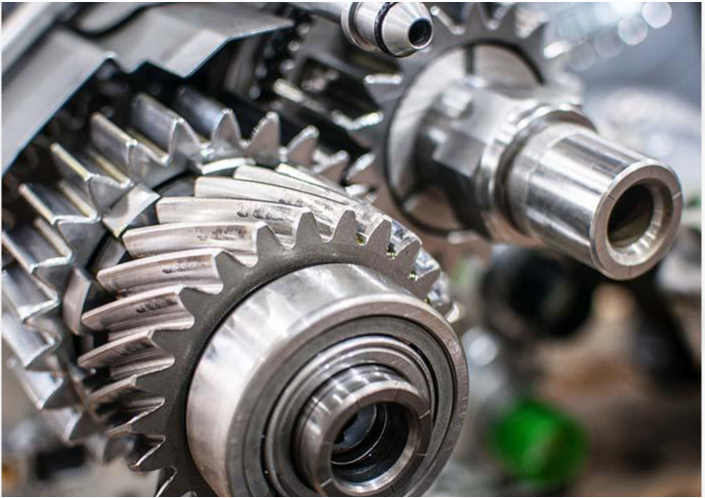 A detailed, close-up photograph of complex mechanical machinery showcasing multiple interlocked silver steel gears, shafts, and a ball bearing component within a transmission assembly.